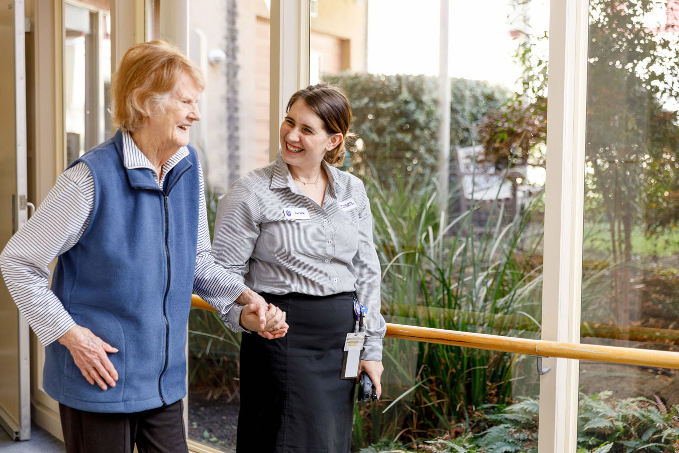 aged care nurse holding hands and walking with a resident