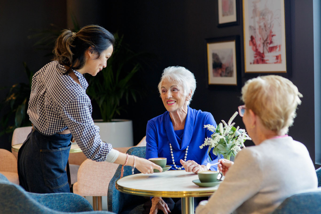 an aged care staff member at kew handing two residents cups of coffee