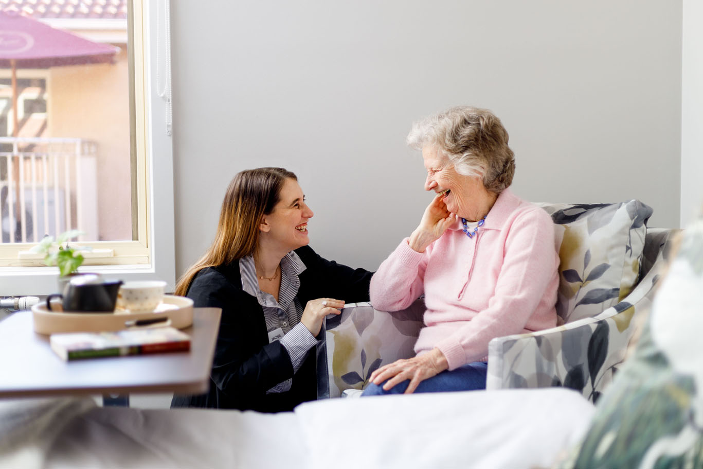 an aged care staff member kneeling down and laughing with a resident in hawthorn